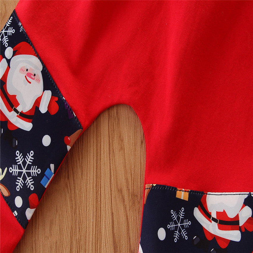 Close-up of a Christmas-themed garment with red fabric and navy blue patches featuring Santa Claus, snowflakes, and presents. The wooden background contrasts with the festive design.