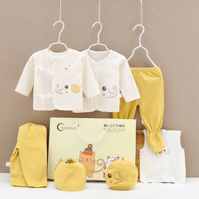Baby clothing set featuring two cream tops with playful faces, mustard yellow pants, matching hats, mittens, and a patterned bib. Displayed with a cute gift bag.