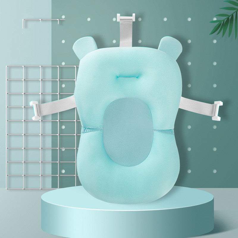 Mint-green baby bath support cushion with white safety straps, positioned on a round platform. Background features a grid, polka dots, and a leaf for decor.