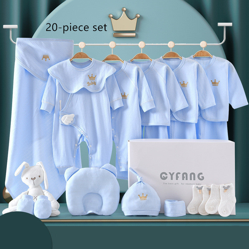Blue 20-piece baby clothing set with onesies, blanket, hat, socks, mittens, pillow, and a plush bunny. Items hang on a rack above a branded gift box with a gold crown motif.