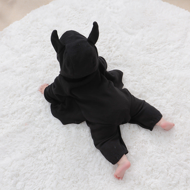 A baby lying on a white fluffy rug, wearing a black bat costume with ears and wings, seen from behind.