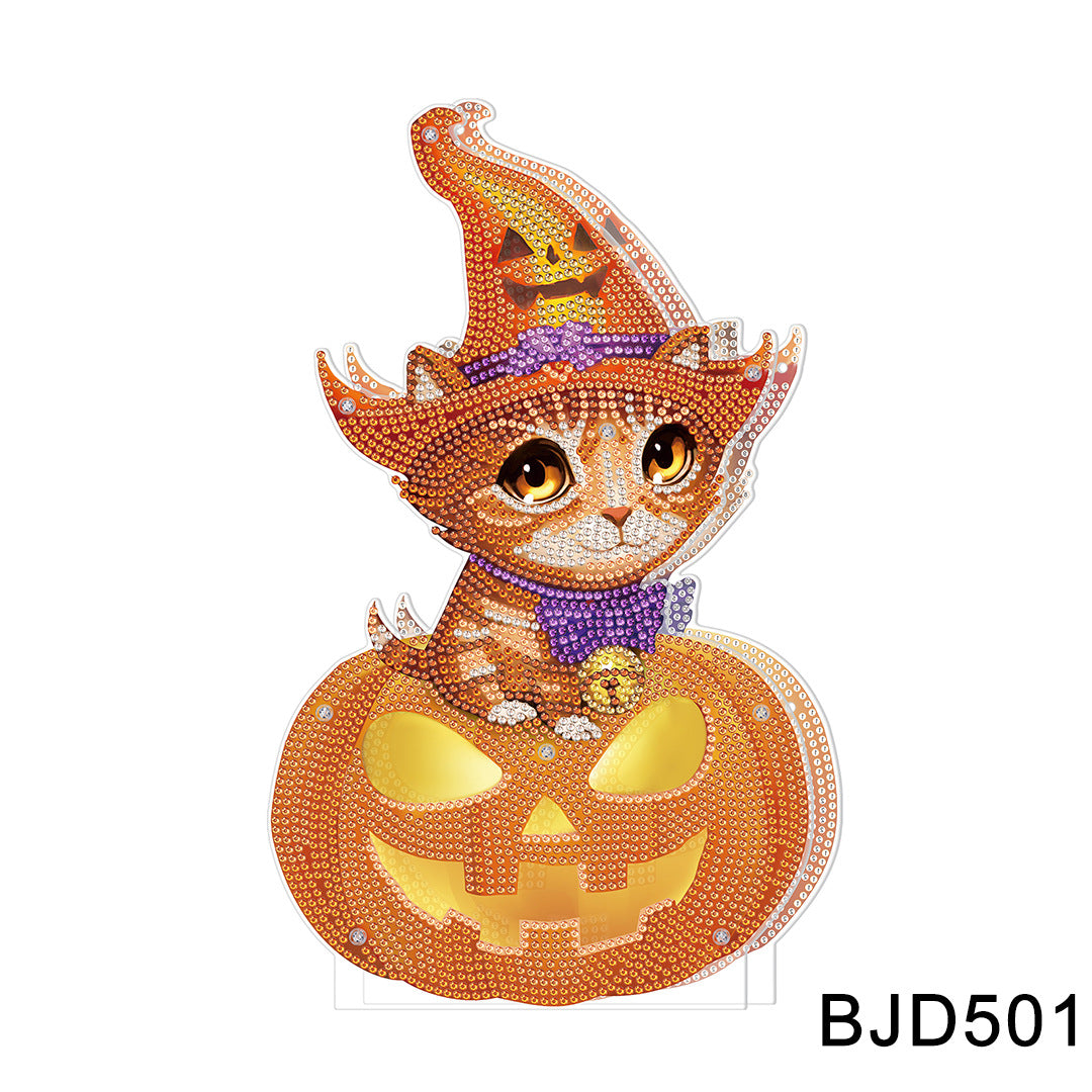 Cute kitten with orange eyes wearing a witch hat and purple bow sits inside a carved pumpkin. The image is composed of small, shiny beads, creating a sparkly effect.