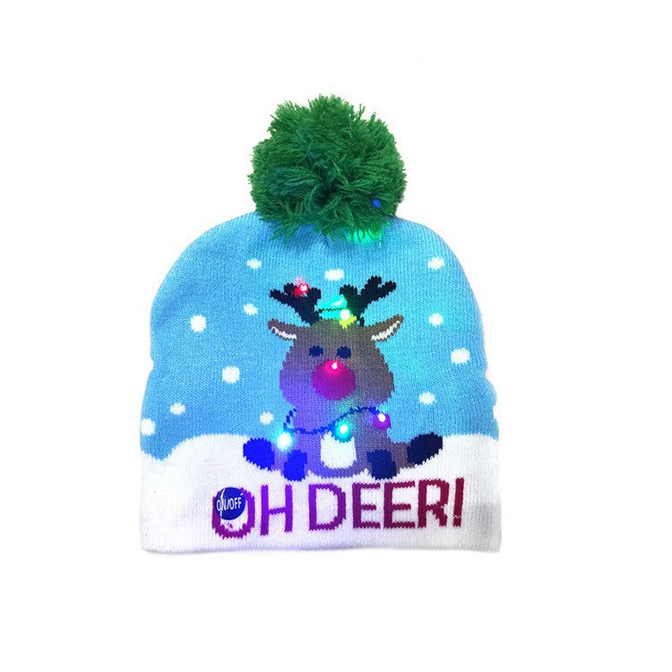 Blue beanie with a green pom-pom features a reindeer with multicolored lights and reads "OH DEER!" against a snowy background. An on/off button is visible.