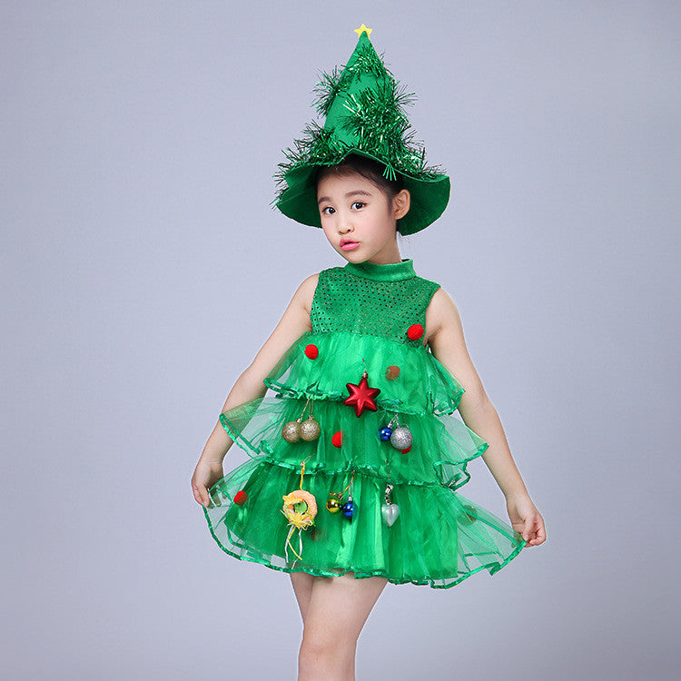 Child in elaborate green dress resembling a Christmas tree, adorned with ornaments. Wearing a matching green hat shaped like a tree top with a star. Neutral background.