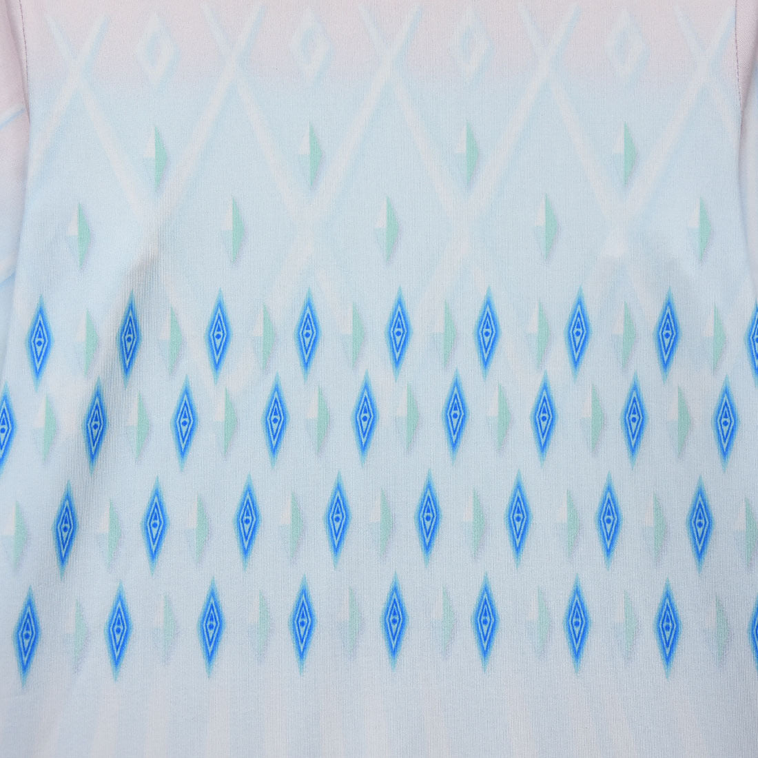 Close-up of a fabric featuring a gradient from white to pink, adorned with a pattern of blue and green diamond shapes arranged in vertical rows.