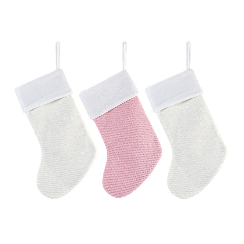 Three Christmas stockings hang side by side. The left and right stockings are white, and the middle one is pink, all with white cuffs and hanging loops.