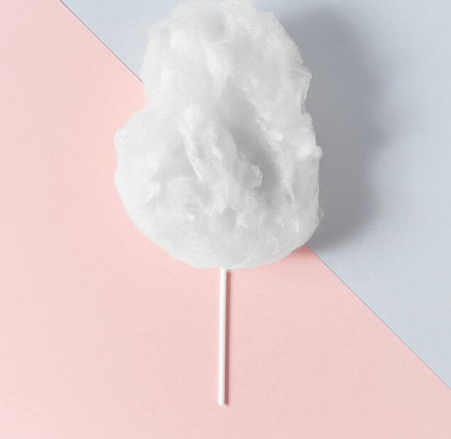 White cotton candy on a stick placed on a pink and gray diagonal background.