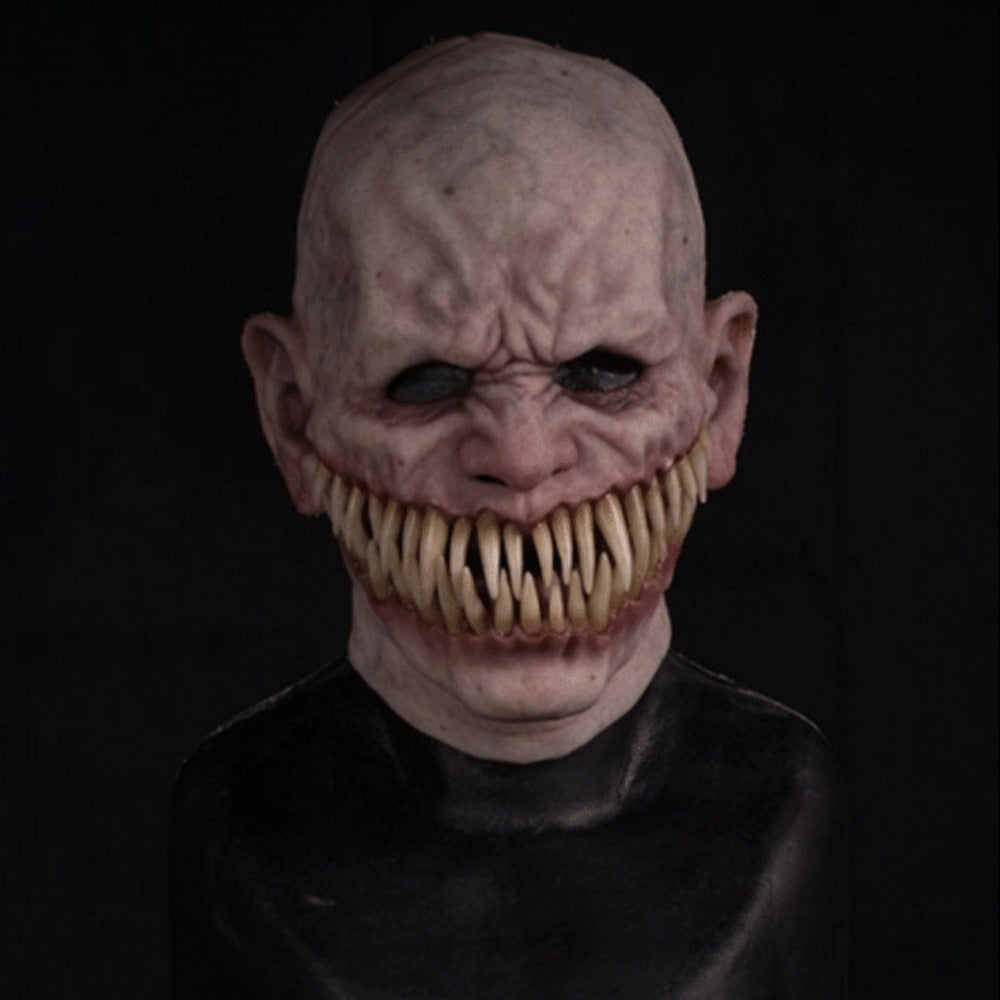 Creepy bald mask with hollow eyes and a wide grin filled with dense, sharp, jagged teeth. The skin appears pale and wrinkled, creating a sinister, monstrous appearance.