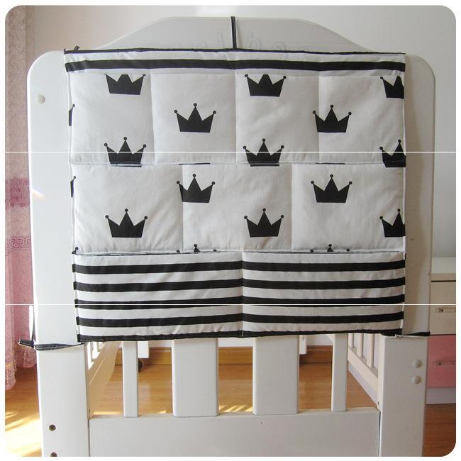 White crib fabric panel with black crown motifs and horizontal black stripes at the bottom, hanging on a white wooden crib in a softly lit room.