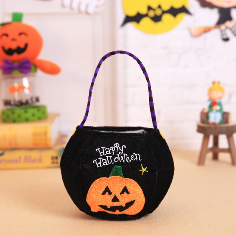 Black Halloween bucket with "Happy Halloween" text and an orange jack-o'-lantern design. Purple and black striped handle. Blurred festive decor in the background.