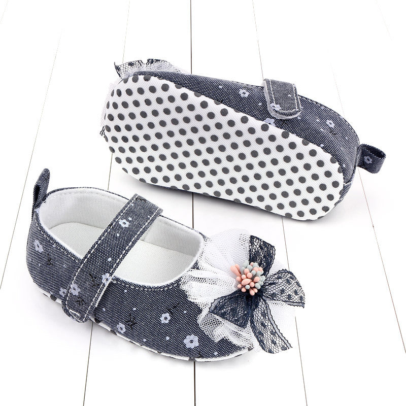 Blue baby shoes with a white floral pattern and delicate bow detail. One shoe is shown from the side, the other from the sole, featuring black polka dots.