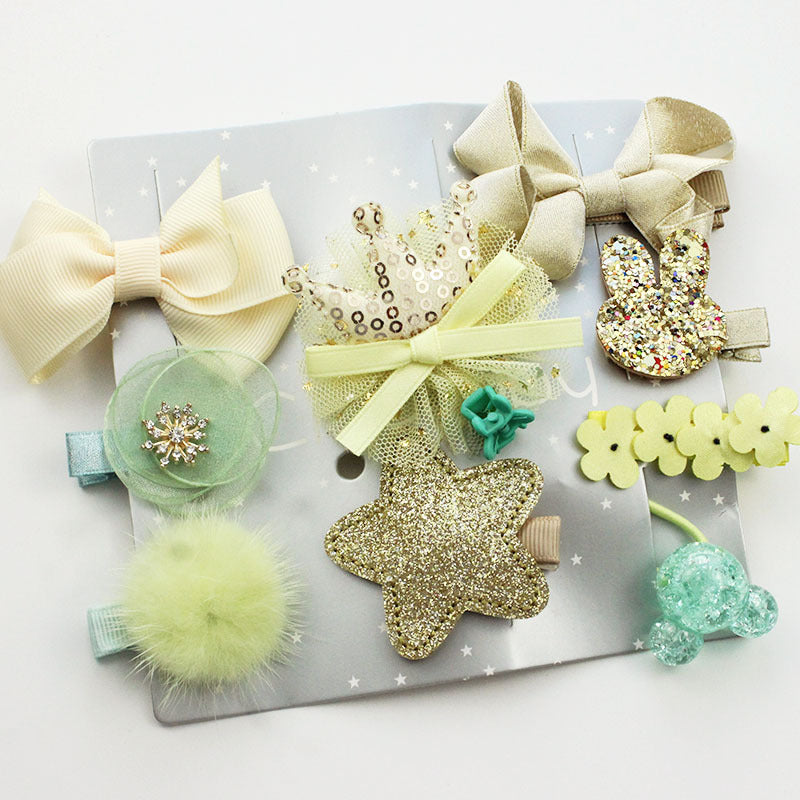 A collection of decorative hair clips on a star-patterned card. Includes glittery stars, bows, a pom-pom, sequined crown, bunny, and floral elements in pastel colors.