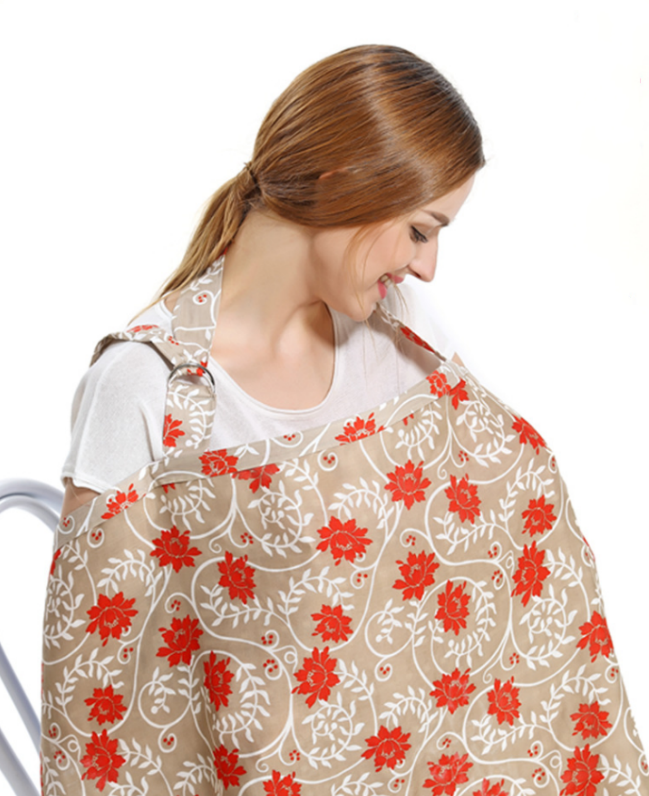 A woman with brown hair smiles while using a floral-patterned nursing cover adorned with red flowers. She is seated against a plain white background.