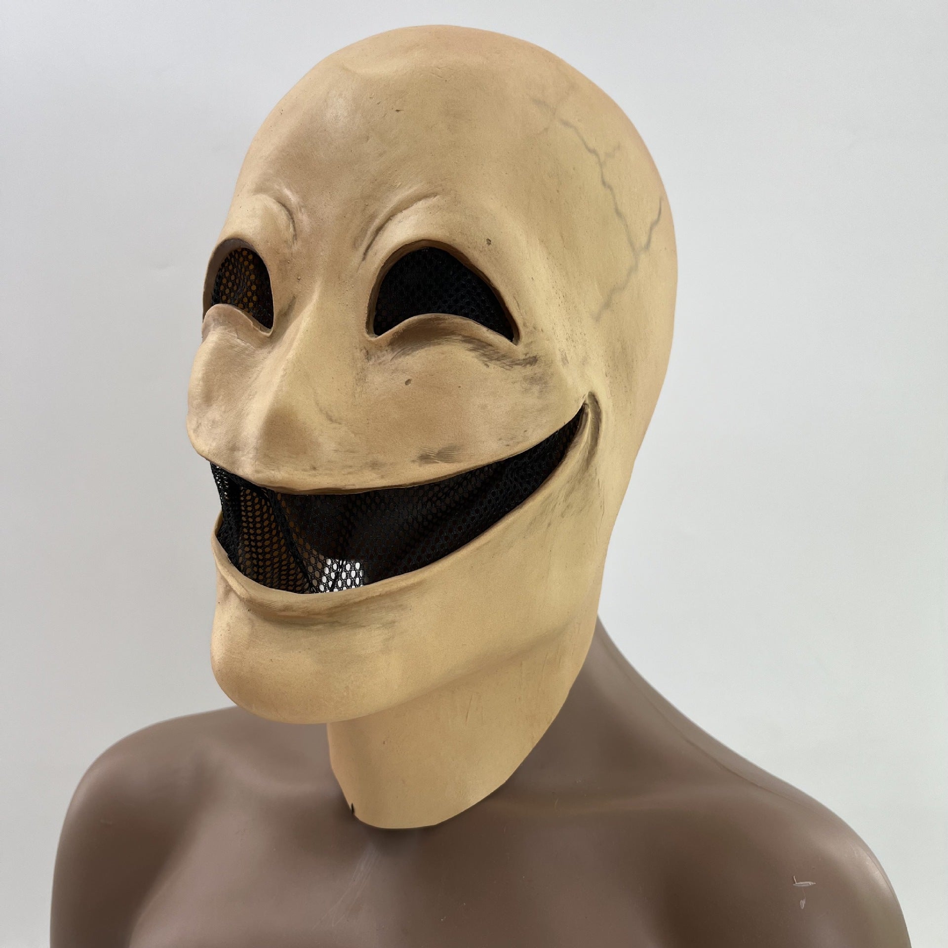 Creepy mask with an exaggerated wide smile, dark eye slits, and a pale, cracked surface. The mask is shown on a mannequin with a neutral background.