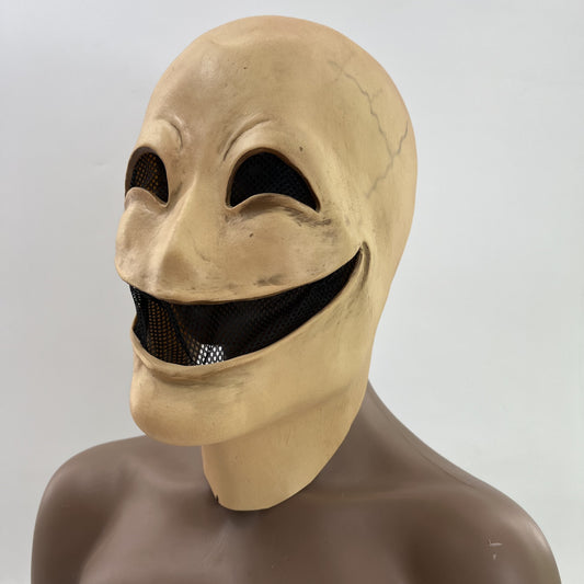 Creepy mask with an exaggerated wide smile, dark eye slits, and a pale, cracked surface. The mask is shown on a mannequin with a neutral background.