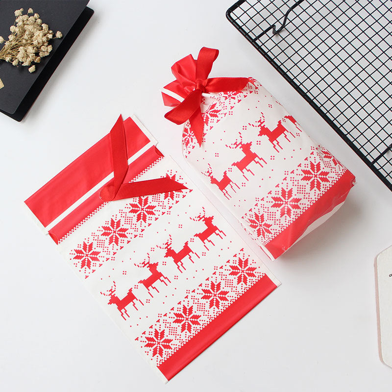 Festive white and red gift wrap with reindeer and snowflakes, featuring a matching ribbon. One gift is wrapped while the other sheet is flat on a white surface.