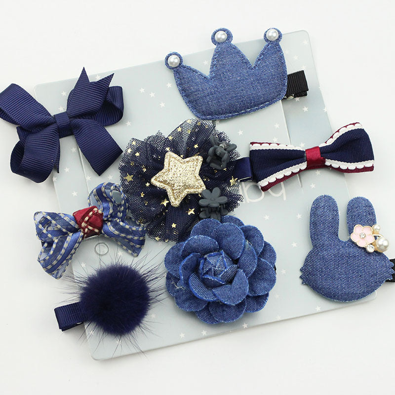 An assortment of blue-themed hair clips and bows, featuring denim textures, a gold star, pearls, and a fluffy pom-pom, arranged on a light background with small stars.