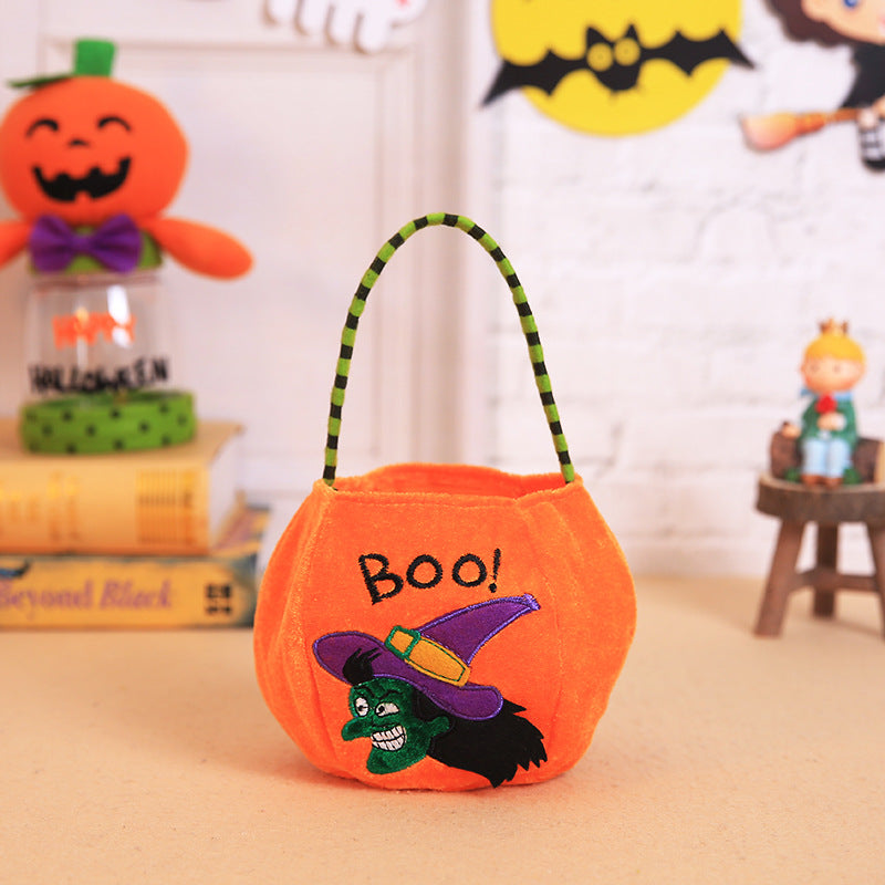 An orange Halloween basket with "Boo!" text and a green witch design. It sits on a table with festive decorations, including a pumpkin figure and a yellow bat sign in the background.