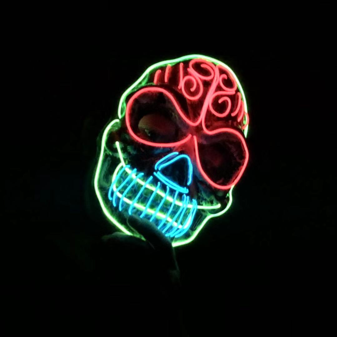 Glowing neon mask with a red, green, and blue skull design against a dark background. The mask features swirls and lines, creating an eerie, luminous effect.