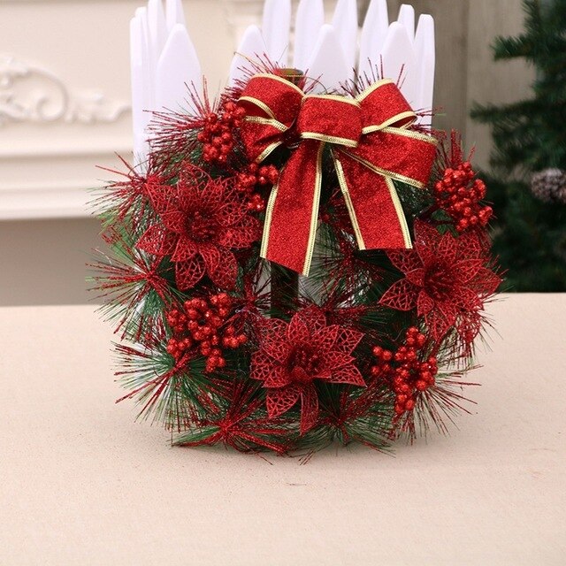 Festive wreath with red poinsettias, berries, and green pine needles, adorned with a large red and gold bow, displayed indoors on a neutral surface.
