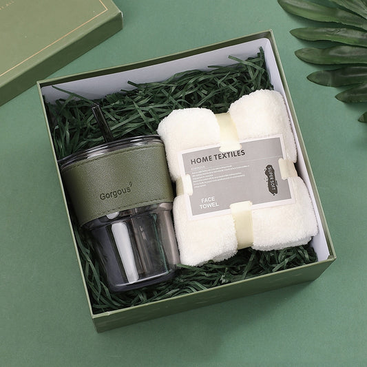 Gift box containing a green travel mug labeled "Gorgous" and a white face towel labeled "Home Textiles," placed on green shredded paper, set against a green background.