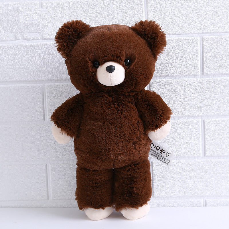 Cute brown teddy bear standing against a textured white wall. It has a plush, fluffy coat, round ears, and a white snout with a smiling expression.