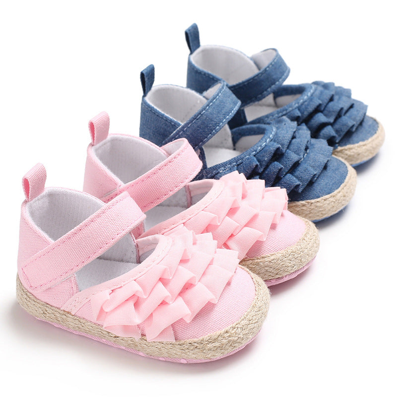 Two pairs of baby shoes displayed side by side; pink shoes with ruffled fronts and blue shoes with similar design, both featuring velcro straps and woven soles.