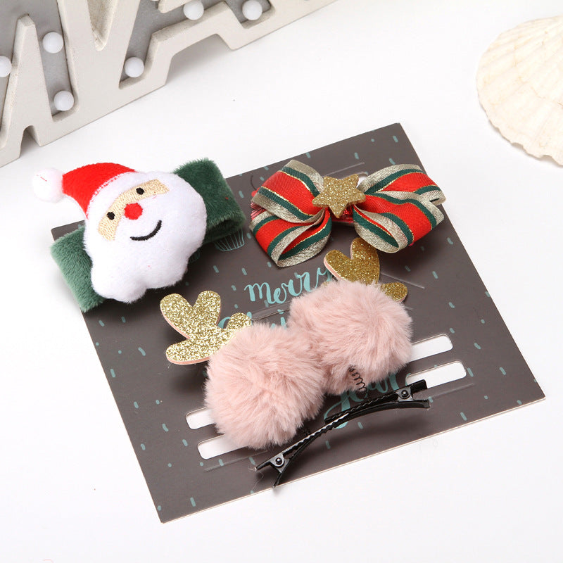 A set of festive hair accessories on a card. Includes a Santa clip, a striped bow with a gold star, and a pom-pom clip with glitter antlers. Background features decorative light-up letters.