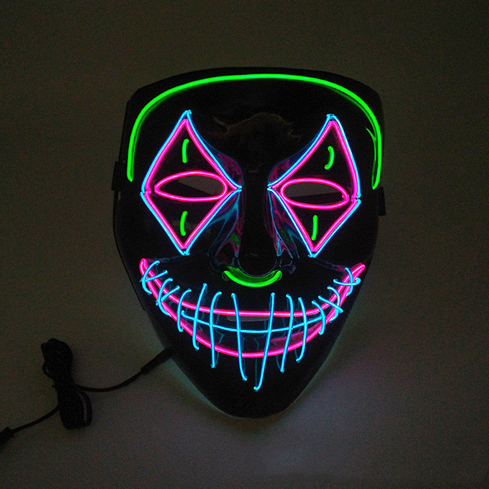 A black mask with neon lights featuring pink diamond eyes, blue stitched mouth, green eyebrows, and nose, glowing in the dark. A power cord is connected on the side.