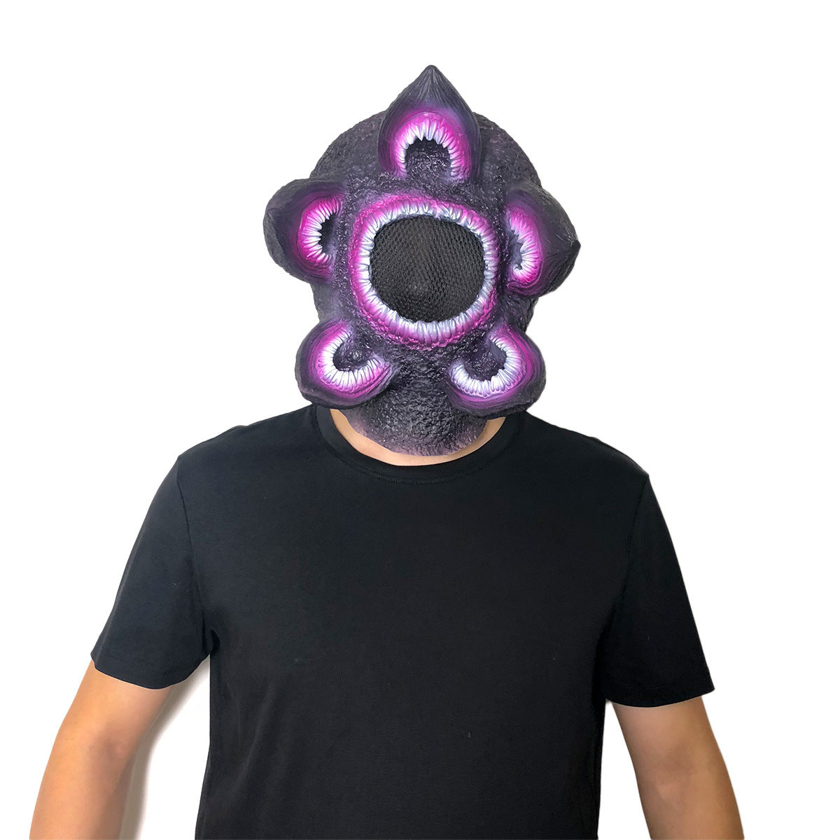 Person wearing a black shirt and a purple, flower-like monster mask with sharp teeth openings against a plain white background.