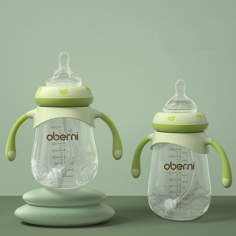 Two transparent baby bottles with green handles and lids are displayed on a green background. One bottle is elevated on a pedestal. Both feature measurement markings and soft nipples.
