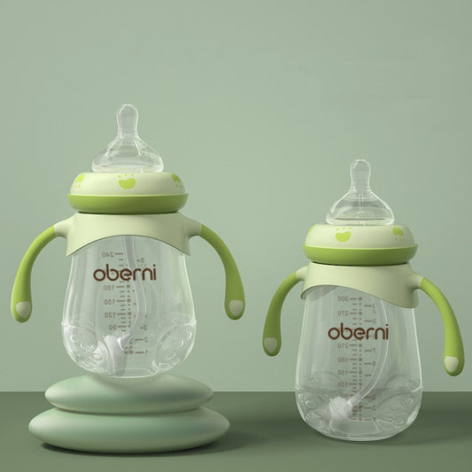 Two transparent baby bottles with green handles and lids are displayed on a green background. One bottle is elevated on a pedestal. Both feature measurement markings and soft nipples.