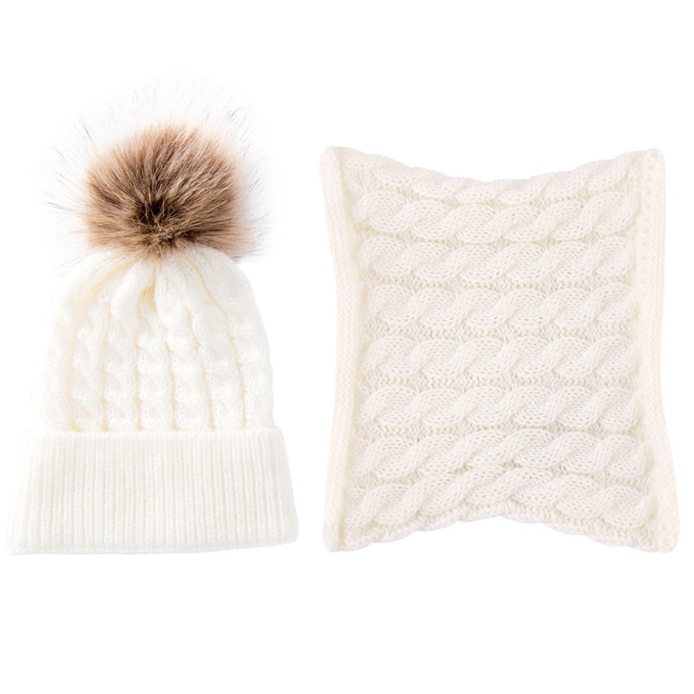 White cable-knit beanie with a faux fur pom-pom next to a matching white cable-knit scarf, both neatly arranged against a plain background.