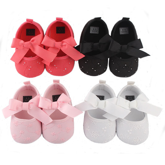 Four pairs of baby shoes in red, black, pink, and white with embroidered patterns and large ribbon bows, arranged in two rows on a white background.