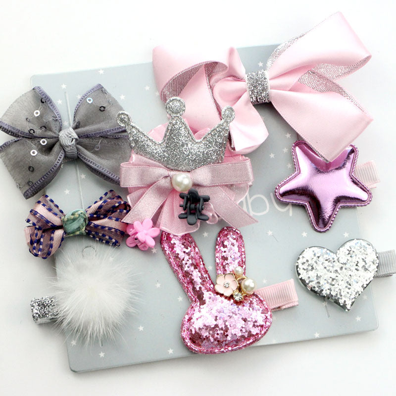 A collection of hair accessories on a light background, including bows, a glittery crown, a pink star, a fluffy pom, and a sequined rabbit shape, adorned with rhinestones and pearls.
