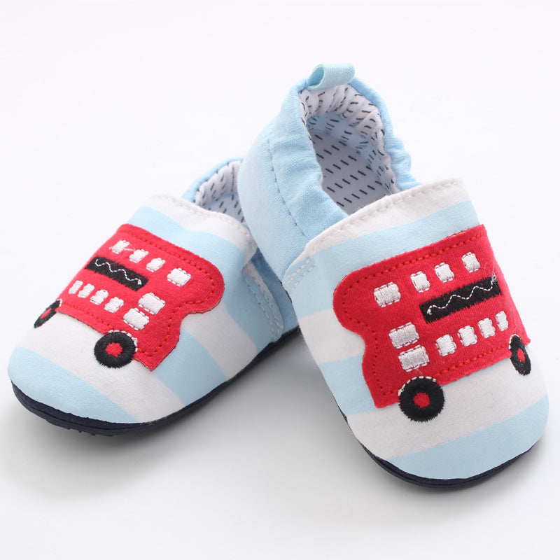 Light blue and white striped baby shoes featuring a red double-decker bus design. They have a soft, elasticized opening and a dotted interior pattern.