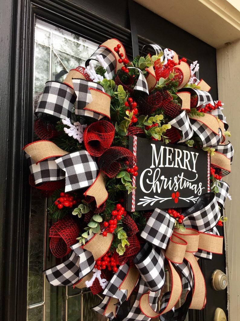 Festive door wreath with black and white checkered ribbons, red mesh, green leaves, and red berries, featuring a "Merry Christmas" sign at the center.