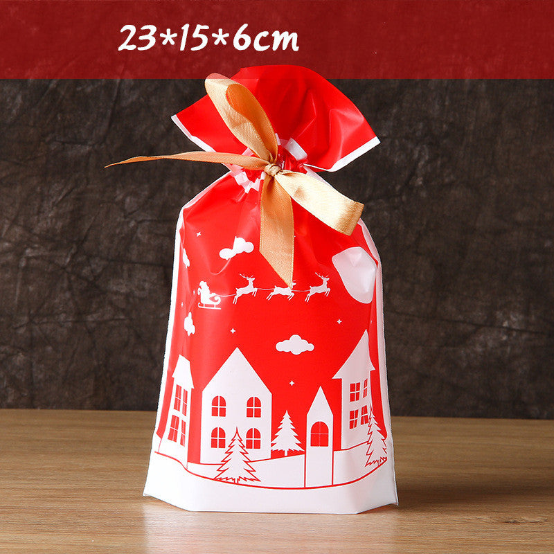 Red gift bag with gold ribbon, featuring white Christmas-themed illustrations of houses and reindeer. Dimensions 23x15x6cm shown above. Placed on a wooden surface.