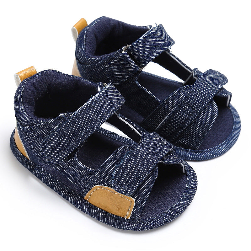 Blue denim toddler sandals with brown accents and adjustable Velcro straps, featuring a soft sole designed for comfort.