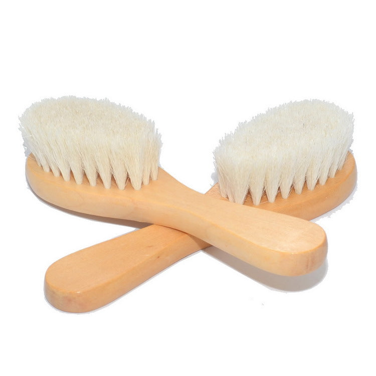 Two wooden baby hairbrushes with soft white bristles are crossed, forming an 'X' shape. The natural wood handles have a smooth finish, contrasting with the fluffy bristles.