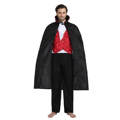 Man in a vampire costume with a red vest, black cape, and fangs, standing barefoot. The cape is open, revealing a white shirt and black pants beneath.