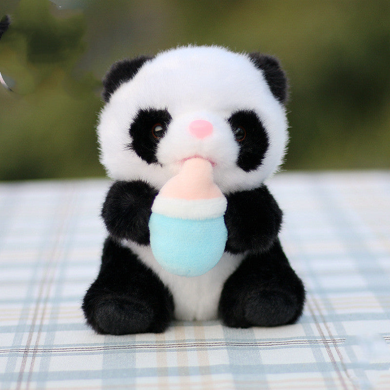 A small plush panda holds a pastel-colored baby bottle while sitting on a plaid surface, with a blurred green background.