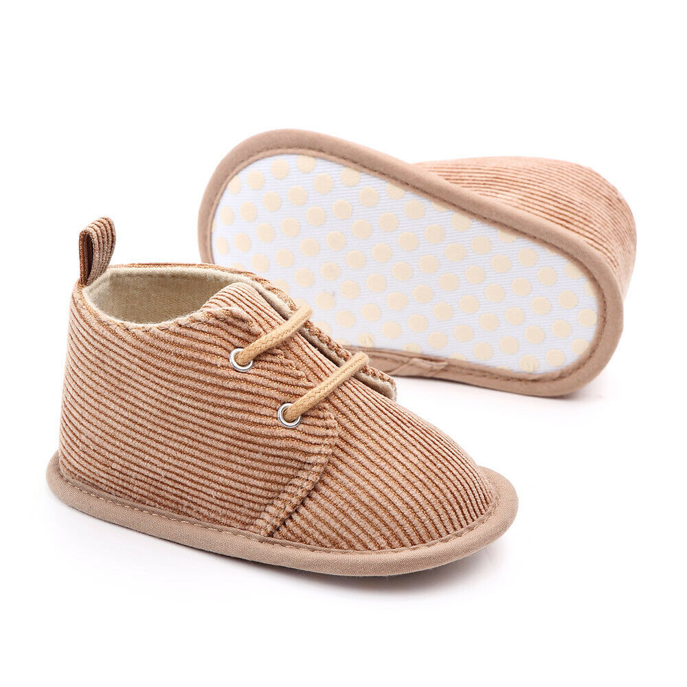 Corduroy baby shoes in light brown, featuring lace-up fronts and a soft, polka-dotted sole. One shoe stands upright while the other lies on its side.