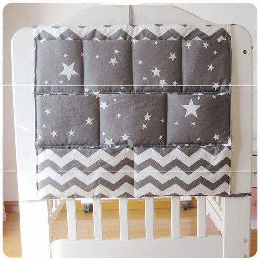 Gray crib organizer hanging on a white chair, adorned with white stars and chevron patterns.