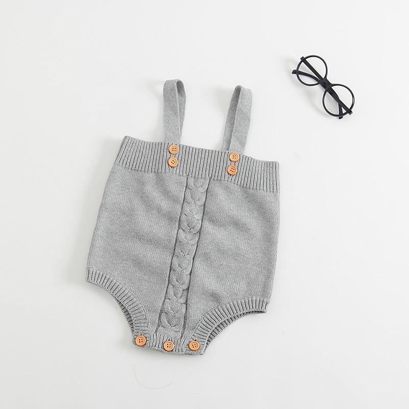 Gray knitted baby romper with cable knit detail, wooden buttons on straps and crotch, lies on a white background next to round black glasses.