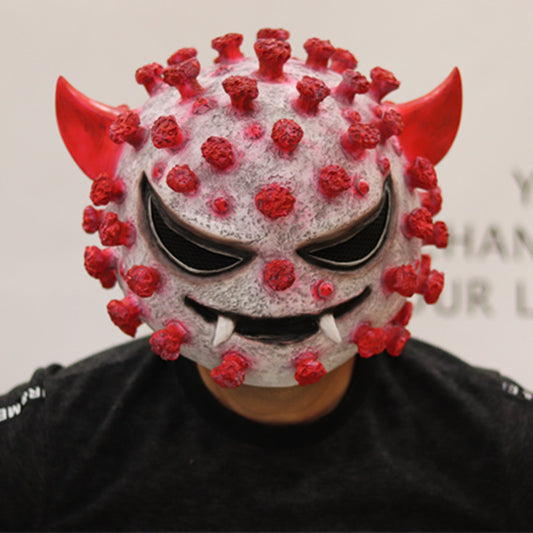A person wearing a creative mask resembling a cartoonish virus with red horns, spikes, and an evil grin. The mask is detailed with a textured surface.
