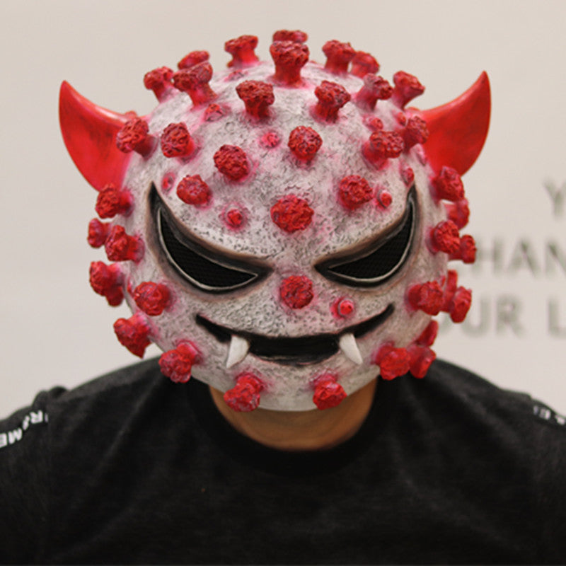 Person wearing a mask resembling a virus with red spikes, horns, and an evil face, combining features of a demon and a virus, against a plain background.