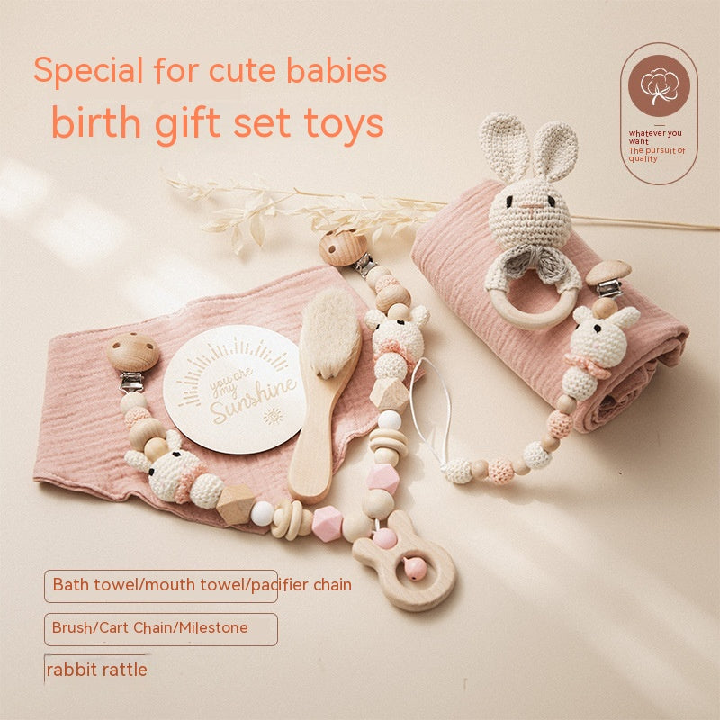 Baby gift set featuring a pink towel, plush rabbit rattle, wooden pacifier chain, soft brush, and milestone card. Text reads: "Special for cute babies, birth gift set toys."