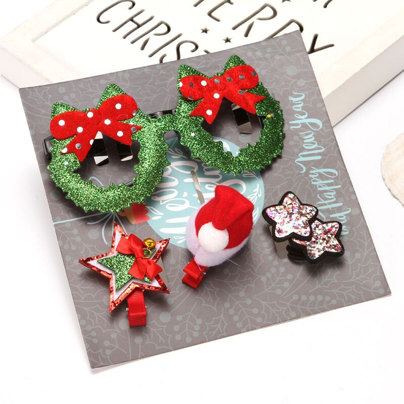 Festive hair accessories on display: green wreath glasses, star clip with red bow, Santa hat clip, and glittery star clips, on a card with holiday designs.