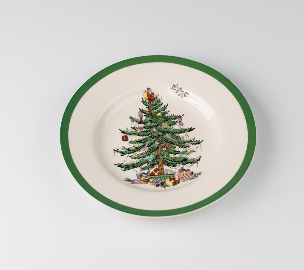 A porcelain bowl with a green rim features a decorated Christmas tree and presents. The tree is adorned with colorful ornaments and a golden star on top.